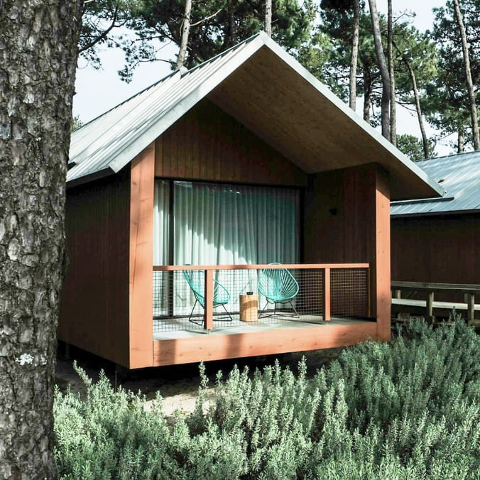 Vista exterior para os bungalows do FeelViana, todos revestidos a madeira e com uma varanda, ideal para momentos de relaxamento. 