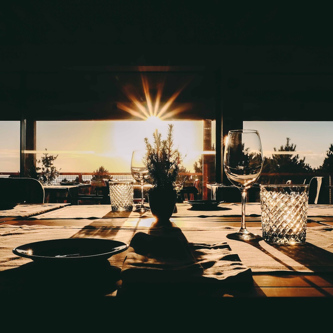 Detalhe de uma mesa do FeelViana Restaurante, com o sol a pôr-se no horizonte e alguns pinheiros como pano de fundo.